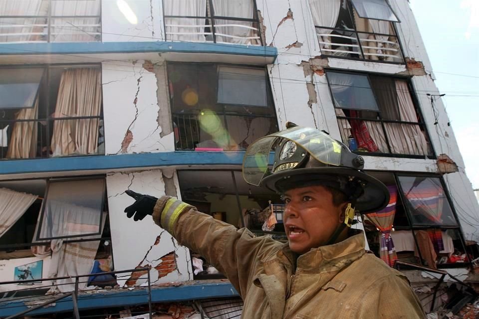 Un bombero señala un edificio con grietas y daños.