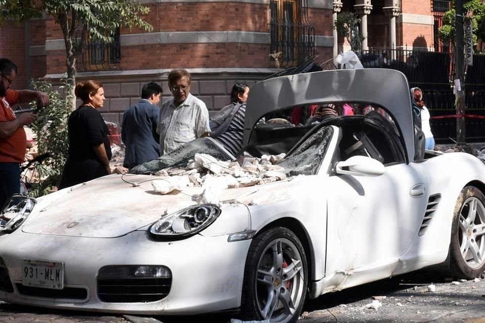 Personas observan un auto dañado tras el sismo.