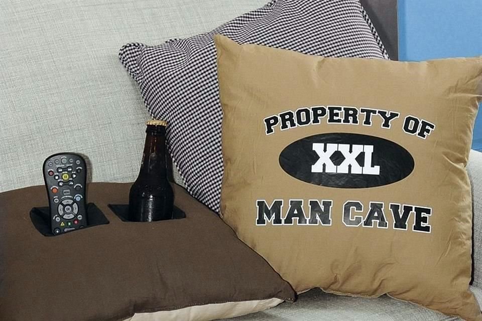 Agrega un toque decorativo en tu sillón con el cojín Man Cave Double Pocket Pillow, el cual cuenta con dos espacios para poner una bebida o el control remoto.<br>Su precio es de 24 dólares.