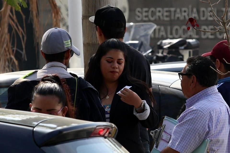 Afuera de la junta, la mujer de saco y el hombre de lentes ofrecen asesoría laboral al hombre de gorra gris.