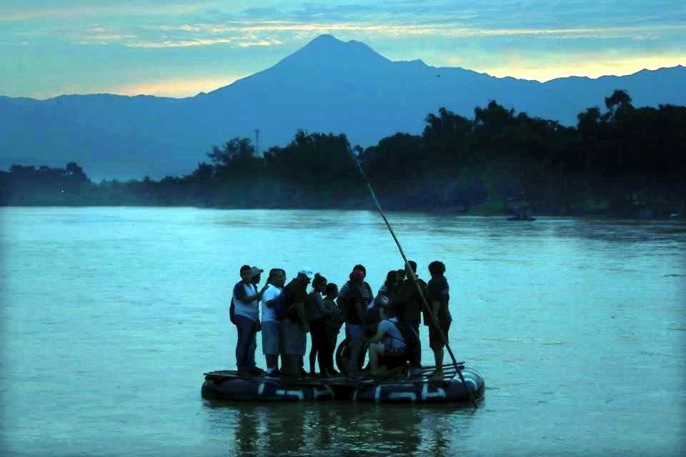 Los migrantes centroamericanos se paran en una balsa para cruzar el río Suchiate de Guatemala a México, con el volcán Tacana al fondo, cerca de Ciudad Hidalgo, México.