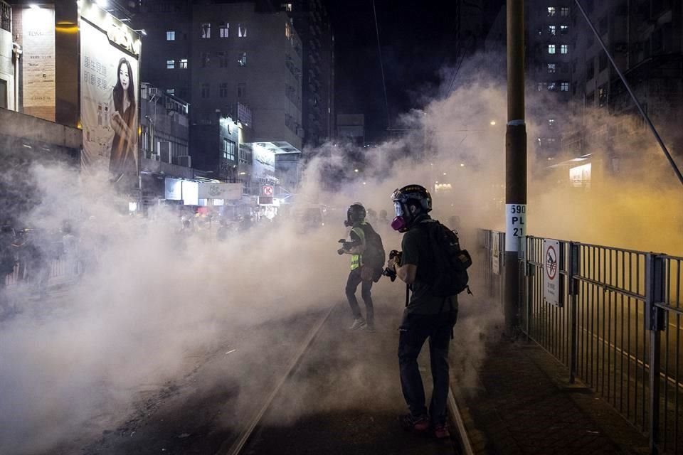 Fotógrafos caminan entre gas lacrimógeno que Policía usó para repeler a manifestantes.