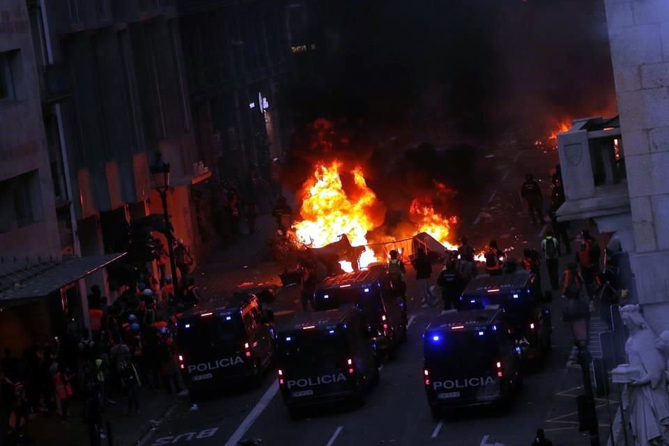 Vehículos de la Policía custodian un área en la que se ve una barricada incendiada.