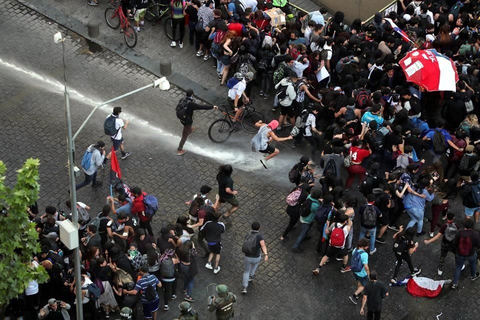 Manifestantes en Santiago se repliegan ante un chorro de agua de las autoridades.