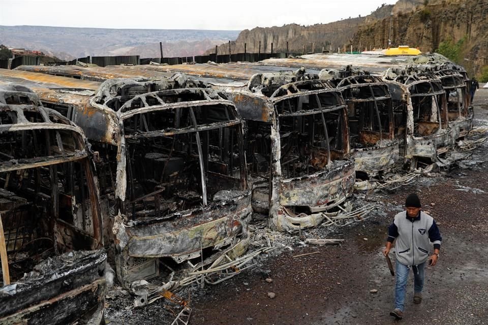 Un hombre camina frente a una fila de autobuses incendiada el domingo durante protestas.