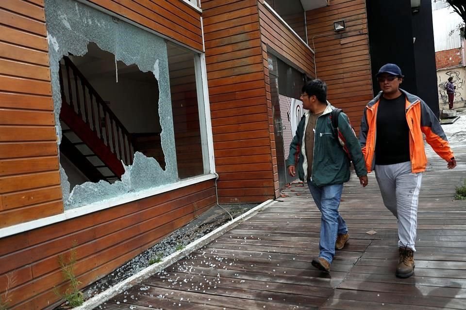 Personas caminan junto a la ventana rota de un restaurante tras los disturbios de ayer.