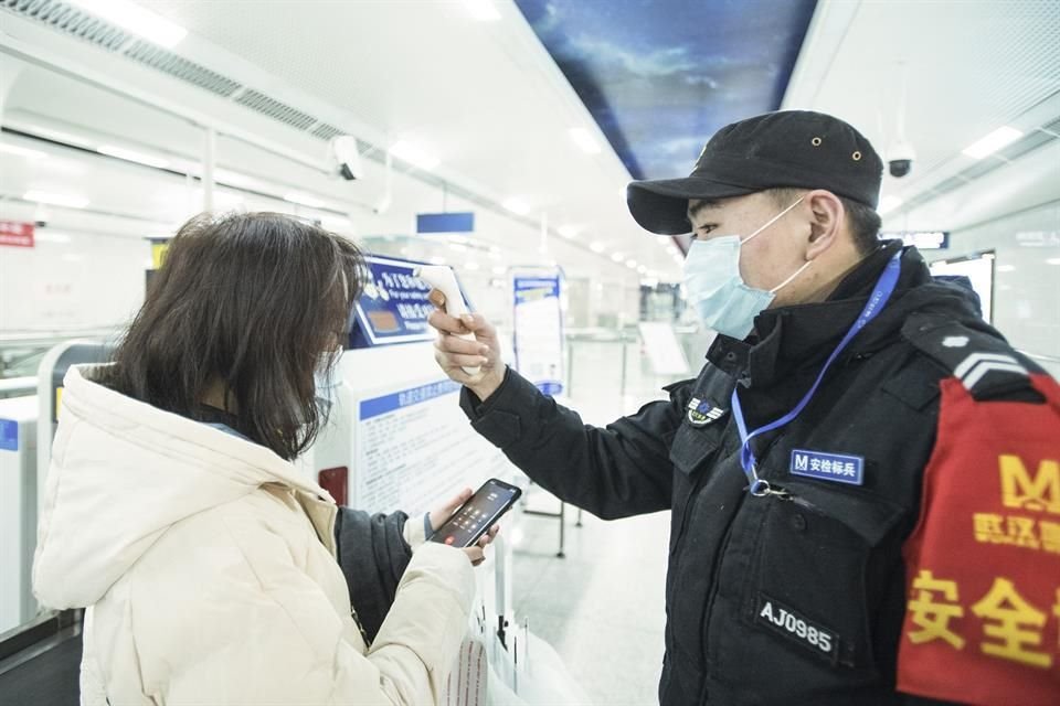 Un empleado checa la temperatura corporal de una pasajera en la estación del metro Wangjiadun en Wuhan.