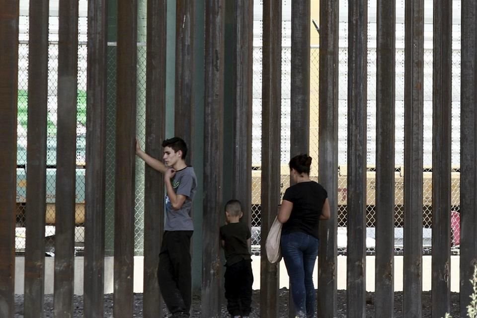 Tres migrantes esperan frente a la frontera con Estados Unidos.