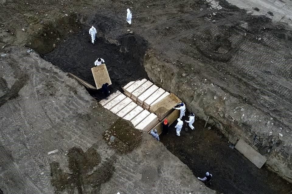 Trabajadores que usan equipo de protección personal entierran cuerpos en una fosa en Hart Island en el distrito de Bronx de Nueva York.