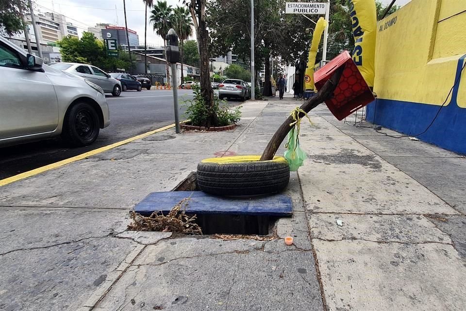 Ante la falta de tapa, un registro en Ocampo alerta a los peatones con una tabla, un tronco, una caja de cerveza y una llanta pintada de amarillo.