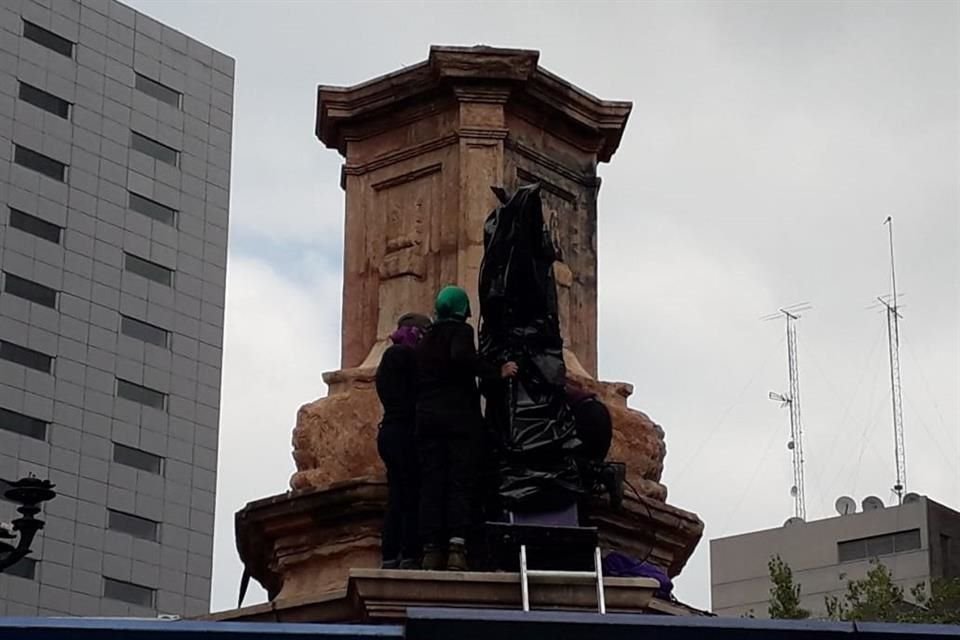 Se trata de una escultura de madera pintada de morado que representa a una mujer con el puño arriba.