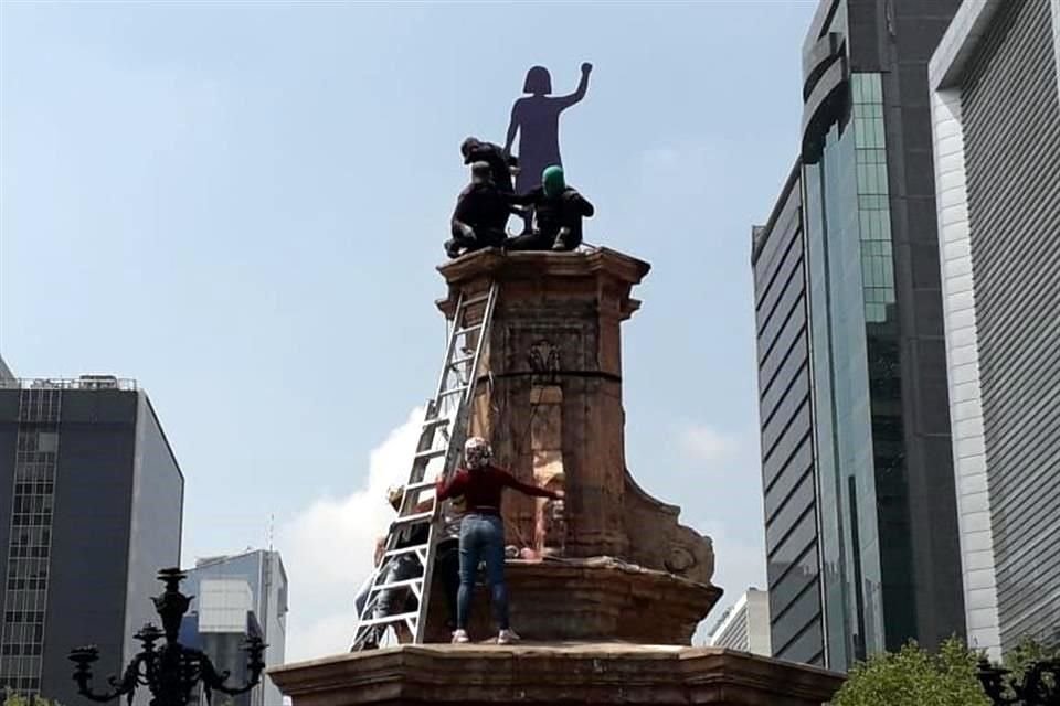 Se trata de una escultura de madera pintada de morado que representa a una mujer con el puño arriba.