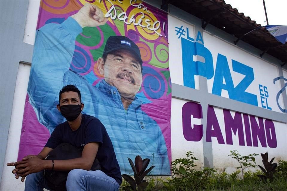 Un hombre en Managua, sentado frente a un mural del Presidente Daniel Ortega, que busca la reelección.