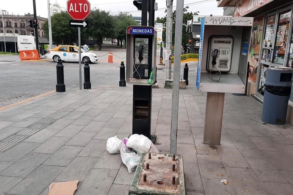 Bolsas de basura sobre la banqueta ampliada, teléfonos públicos en desuso y una base abandonada afean la zona.