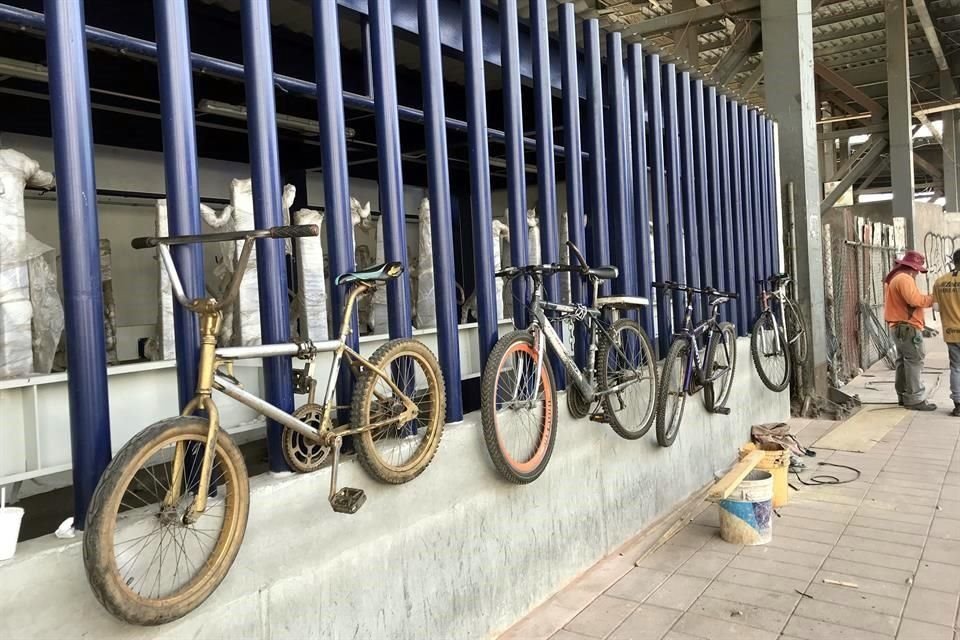 Usuarios cuelgan sus bicis en tubos de acero en la parte externa del biciestacionamiento que está cerrado.