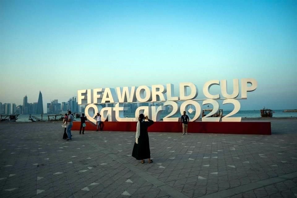 Visitantes se toman fotos junto a un anuncia de la Copa Mundial de Futbol, en Doha.