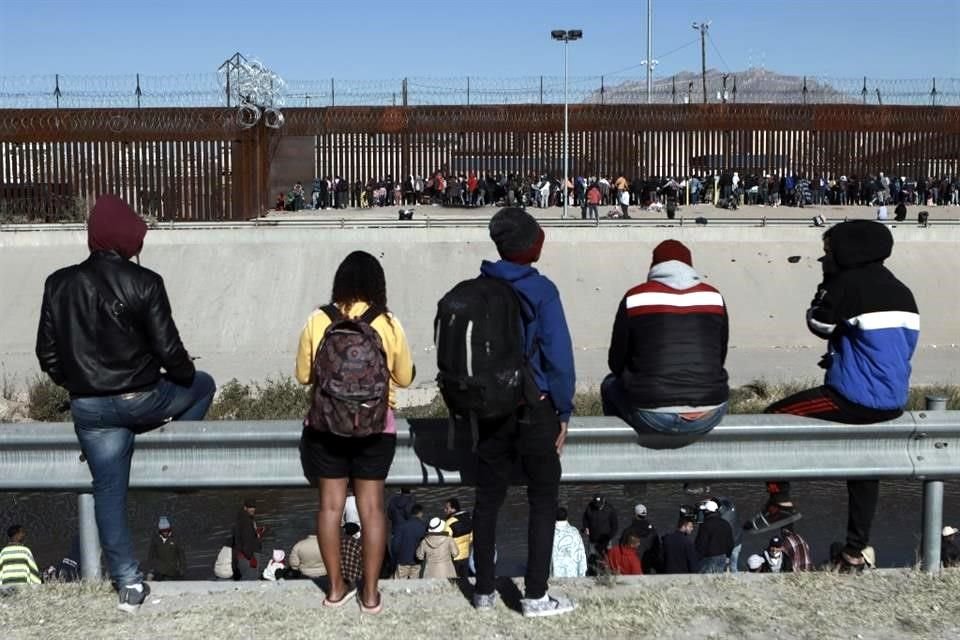 Varios migrantes observan a otros junto a la valla fronteriza en Ciudad Juárez, México.