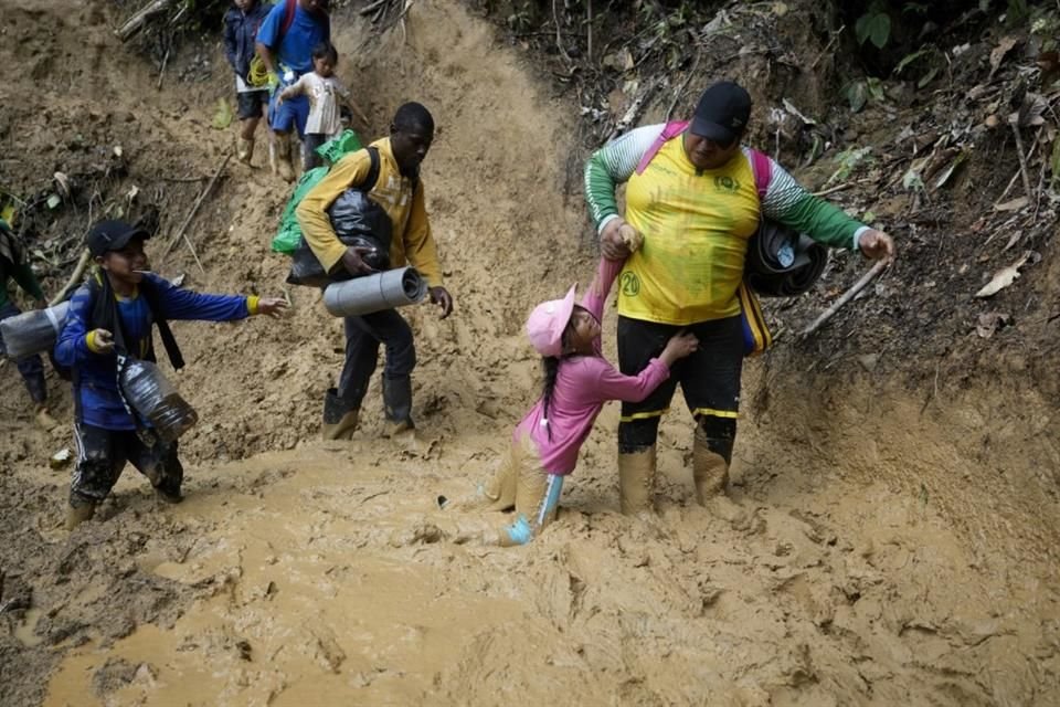 Una mujer trata de levantar a una niña de un paso enlodado mientras migrantes ecuatorianos atraviesan la selva del Darién.