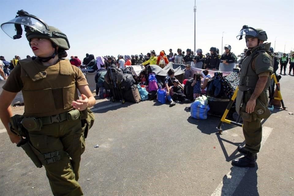 Carabineros al lado de migrantes sentados en una carretera cerca de Arica, Chile.