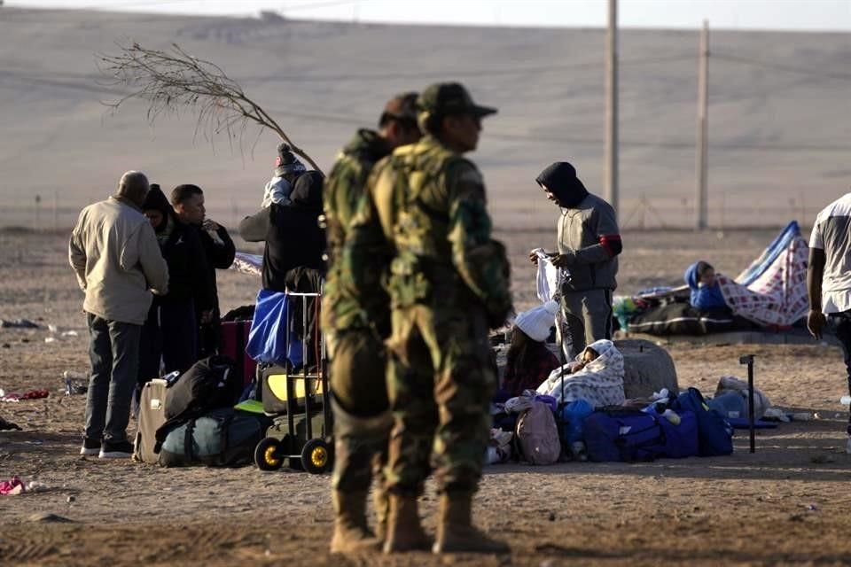 Una familia migrante acampa en la frontera peruana con Chile, sin poder cruzar, mientras la policía de las fuerzas especiales vigila en Tacna, Perú.