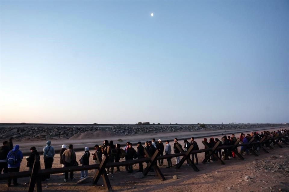 Migrantes que buscan asilo en los Estados Unidos esperan en fila bajo la luna antes del amanecer para ser procesados por agentes de la Patrulla Fronteriza.