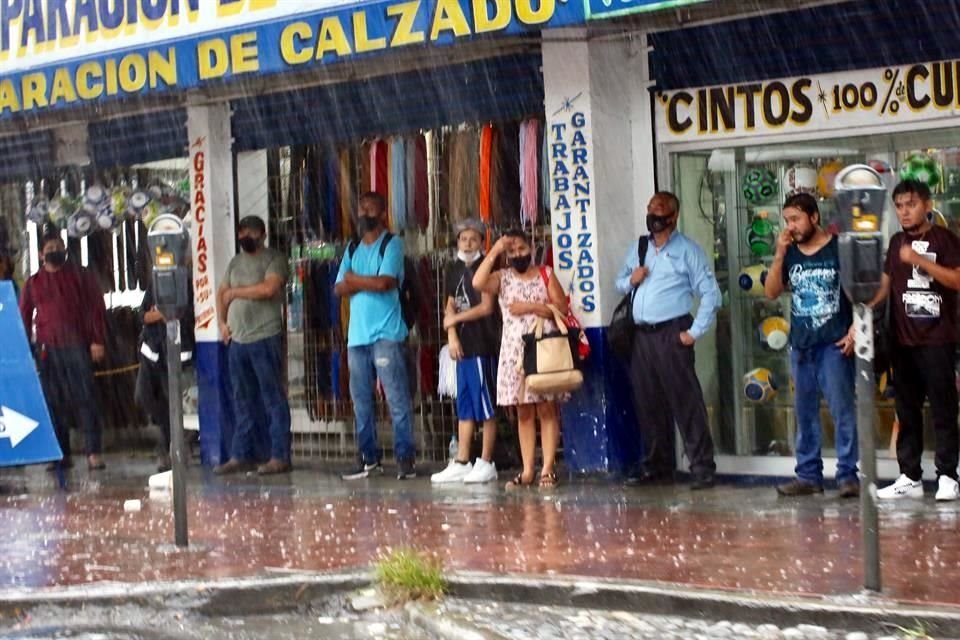 Algunas personas buscaron cubrirse de la lluvia frente a negocios, en el Centro.