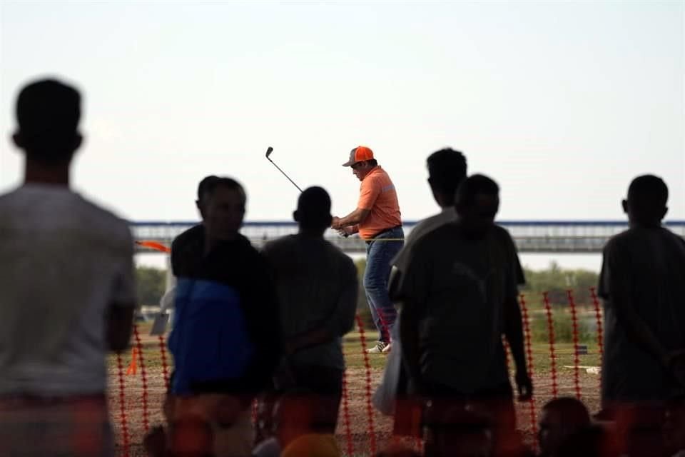 Migrantes observan a un golfista del lado estadounidense practicar su deporte en un campo cerca del Río Bravo.