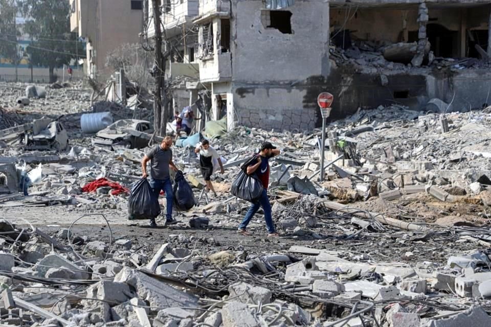 Personas caminan frente a edificios destruidos en la Ciudad de Gaza.