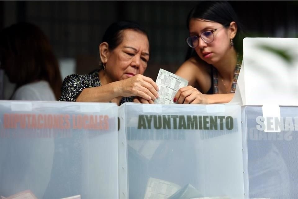 Una joven orienta a una electora para introducir correctamente sus boletas en las urnas.