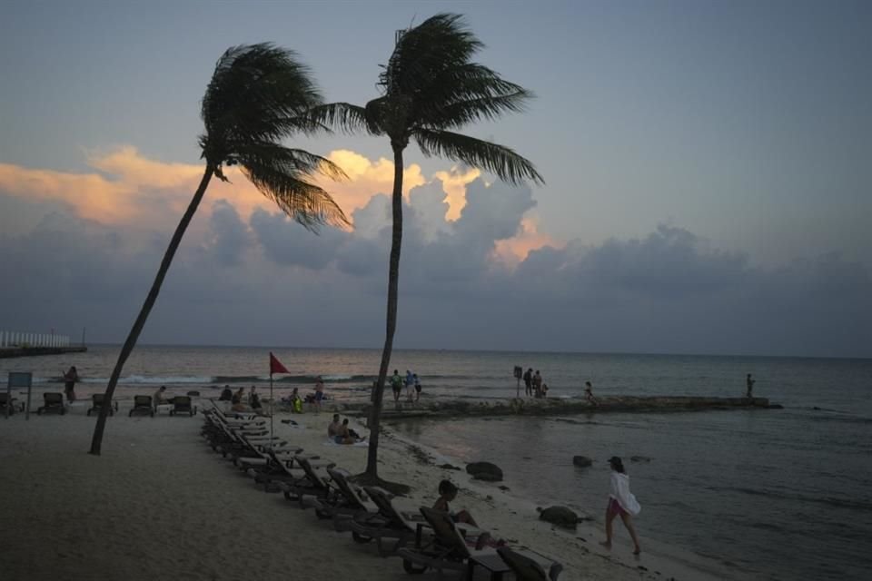 Gente en la playa mientras se pone el sol antes de la llegada del huracán Beryl en Playa del Carmen, México.