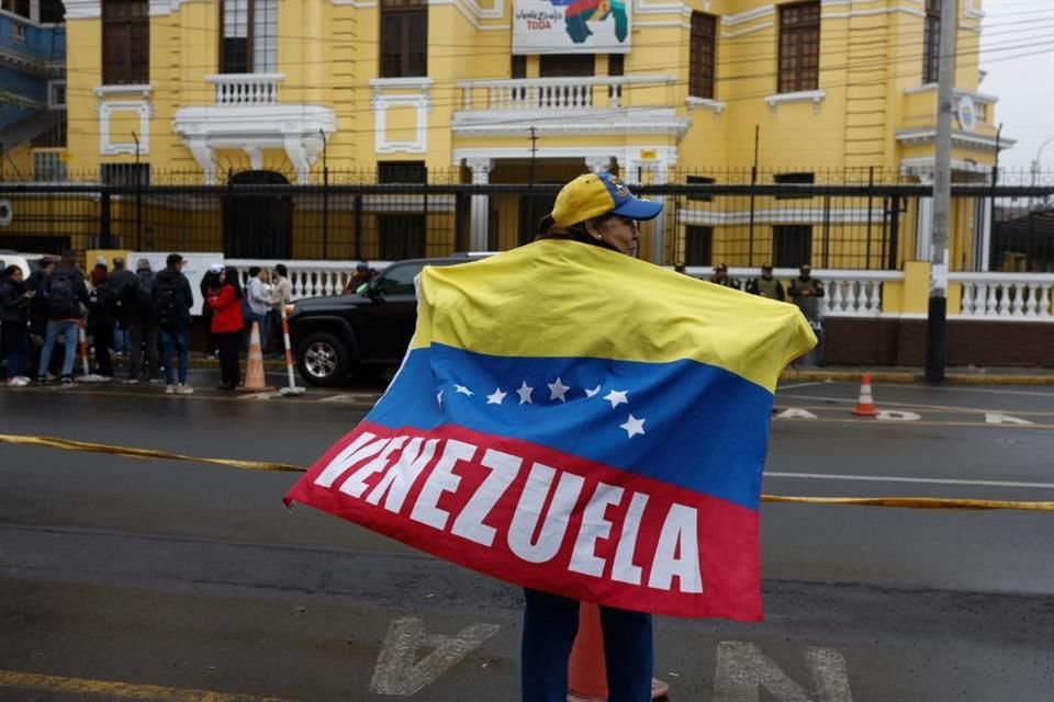 Una mujer sostiene una bandera de Venezuela afuera de la Embajada de Venezuela en Lima.