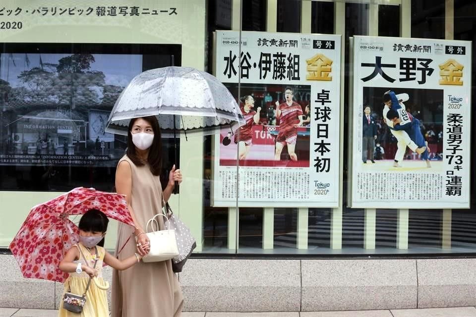 Una mujer y una niña con cubrebocas caminan por las calles de Tokio junto a periódicos reportando los eventos de los Juegos Olímpicos.