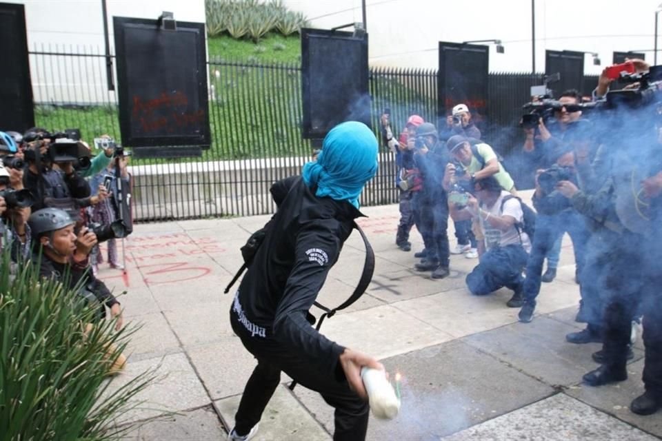 Otro estudiante de Ayotzinapa se prepara para lanzar un petardo desde las afueras del Senado.