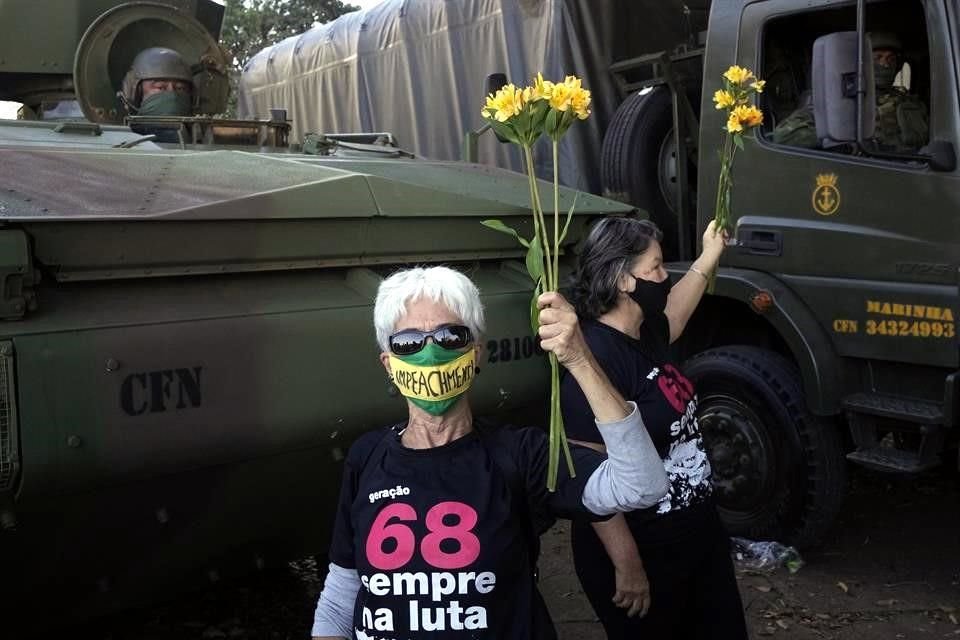 Una mujer con un cubrebocas que dice 'juicio político' sostiene flores que entregó después a los militares en señal de oposición a Bolsonaro.
