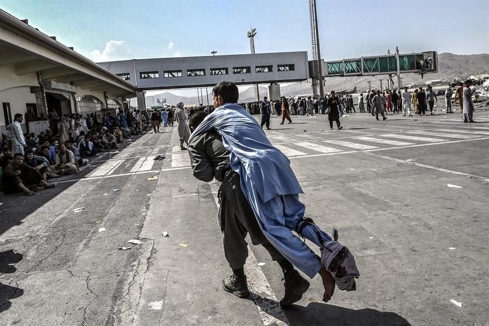 Una persona carga a un herido en el aerupuerto de Kabul, mientras otras personas hacen filas intentando abordar un avión.