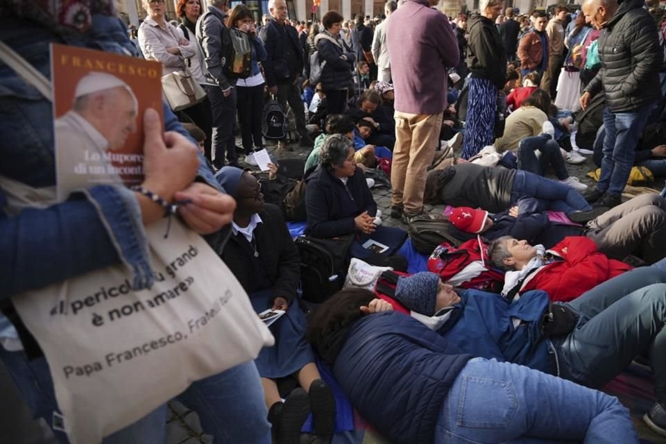Fieles descansan en el piso afuera de la Basílica de San Pedro, en espera del funeral del Papa Francisco.