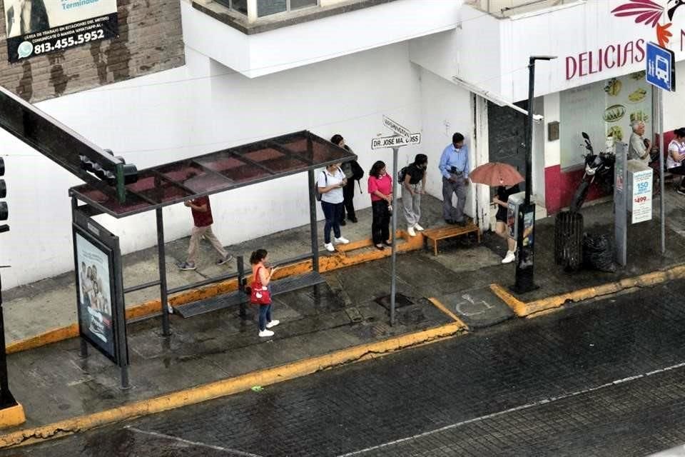 Usuarios del transporte público se protegieron en donde pudieron ante la lluvia mientras esperaban el camión.