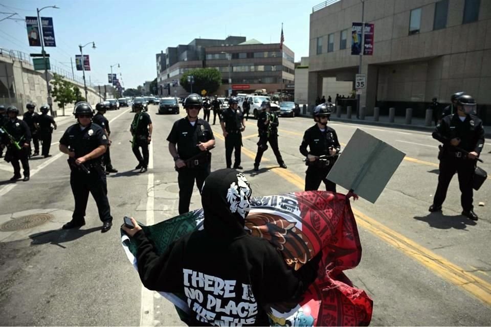 Una persona ondea una bandera frente a agentes de policía en una manifestación para protestar contra las operaciones federales de inmigración en Los Ángeles.