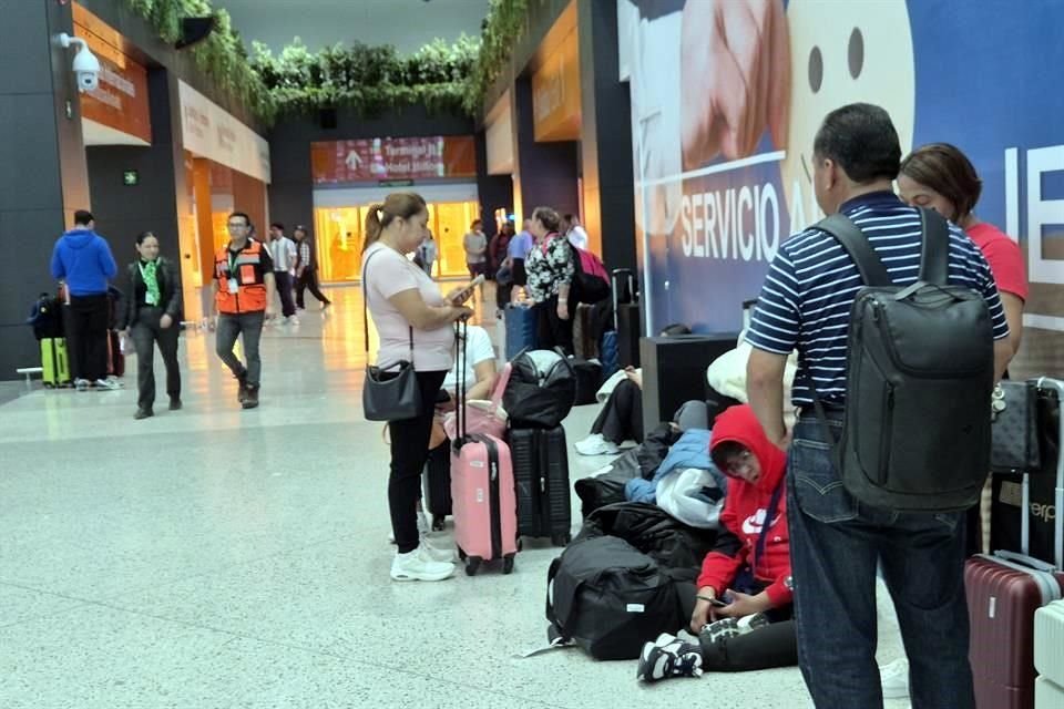 En la Terminal A del Aeropuerto, visitantes y viajeros se sientan en el suelo, mientras esperan a familiares.