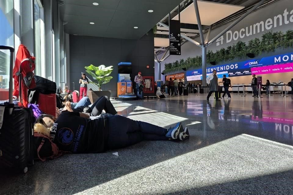En la Terminal A del Aeropuerto, visitantes y viajeros se sientan en el suelo, mientras esperan a familiares.