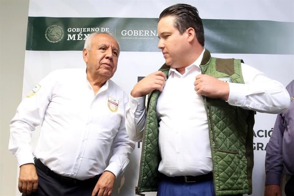 Daniel Torres se pone un chaleco con logo del INM, junto al Comisionado del organismo, Francisco Garduño.