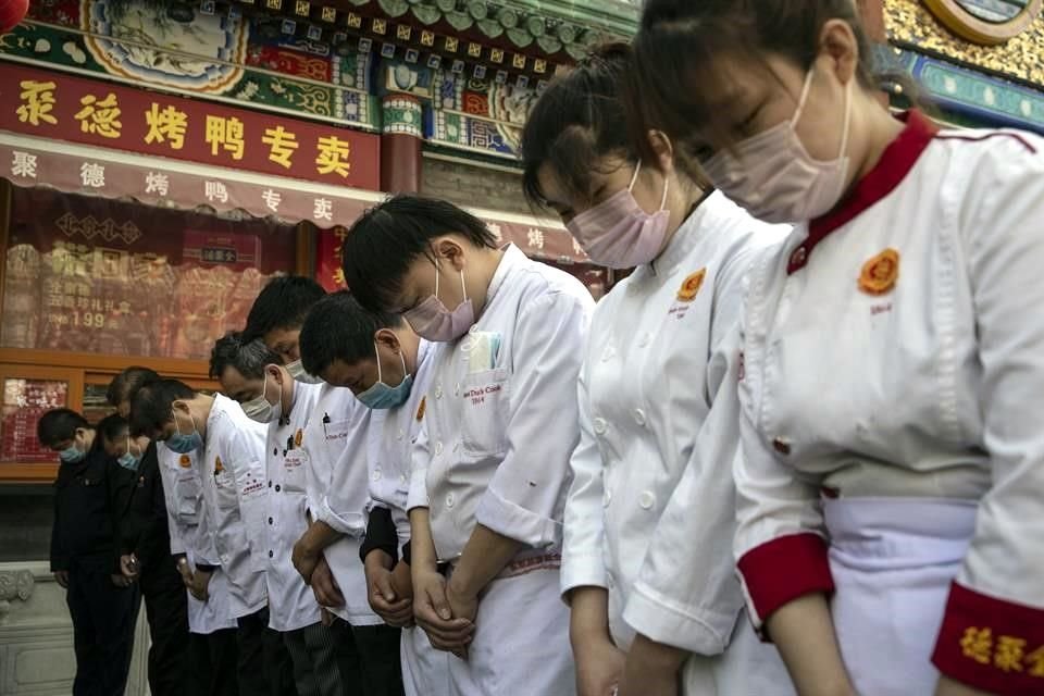 Empleados de un restaurante se reúnen en una calle de Beijing para participar en la ceremonia en honor a las víctimas de Covid-19.