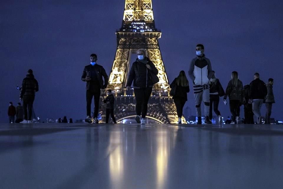 Personas con cubrebocas caminan cerca de la Torre Eiffel al anochecer, pocas horas antes de que entre en vigor el toque de queda nocturno en toda la ciudad en París.