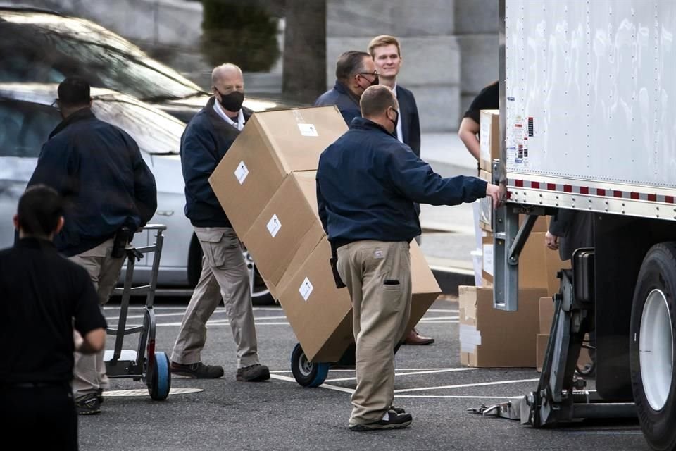 Trabajadores cargan cajas en un camión de mudanza afuera de la casa blanca.