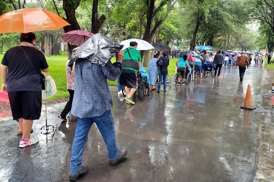Cientos de beneficiarios, muchos en silla de ruedas, traen encima bolsas de plástico y se cubren con un paraguas.